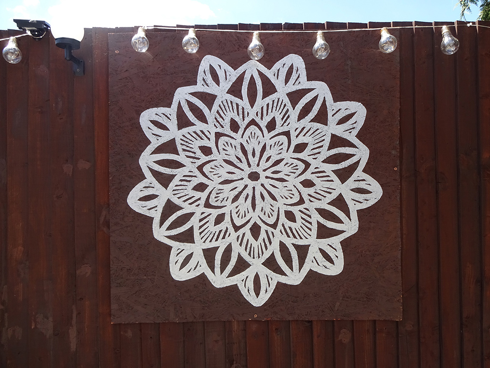 A hand painted mural, a mandala painted onto a fence.