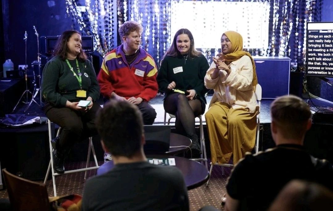 Image of Four people sitting at the front of a room, talking