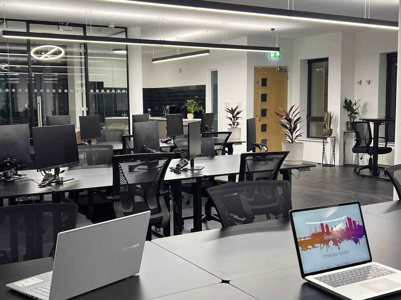 An image of a three banks of 8 desks in the iungoworks coworking space with meeting rooms and a communal kitchen in the distance