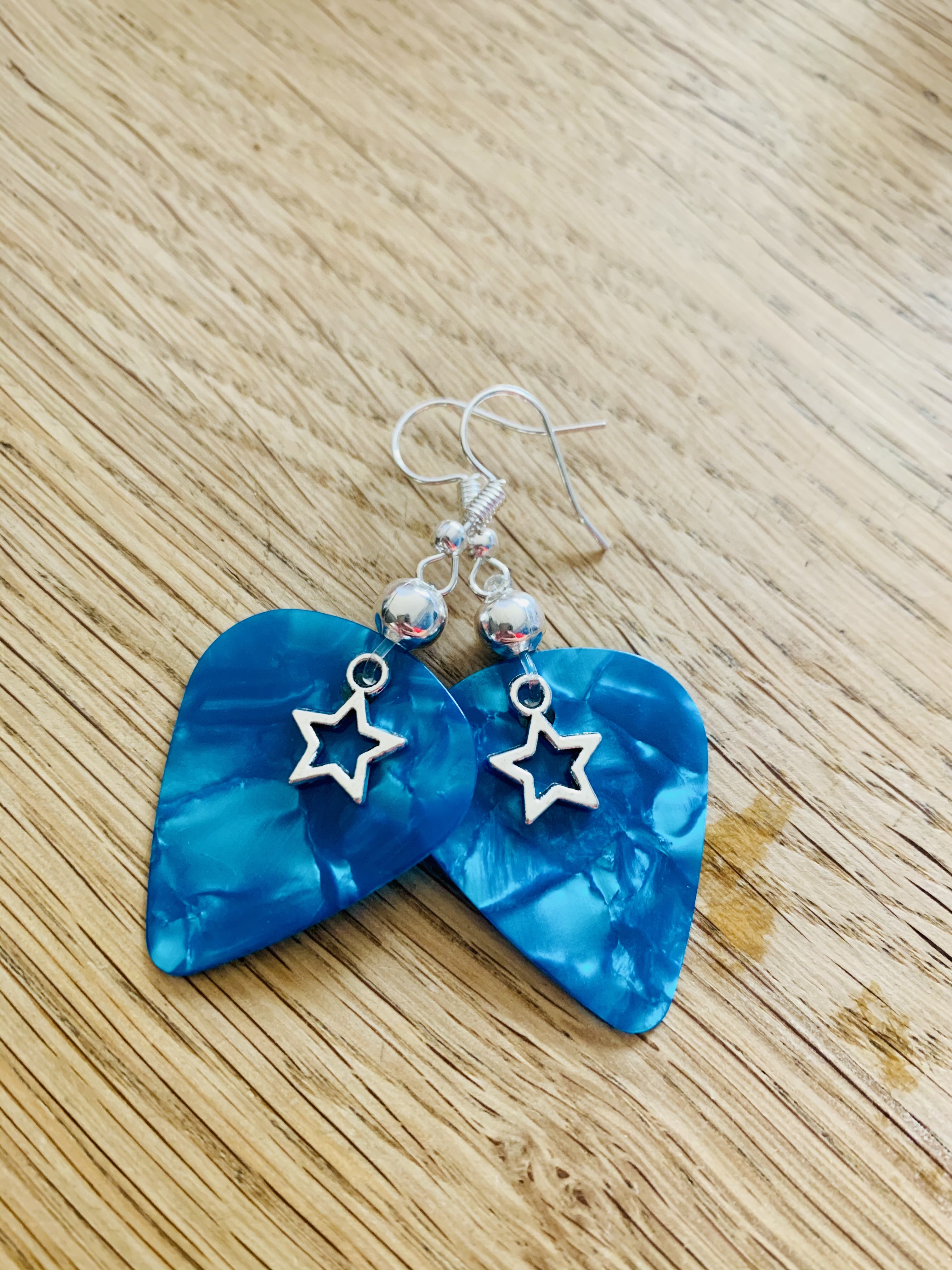 Pair of blue marbled resin earrings in triangular shape with silver star charms and silver beads, displayed on light wood surface