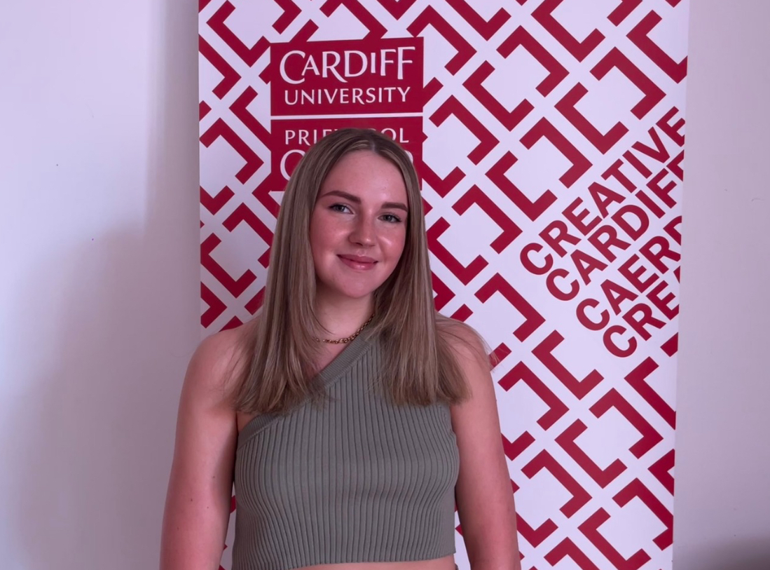 Image of Katie smiling next to the Creative Cardiff banner