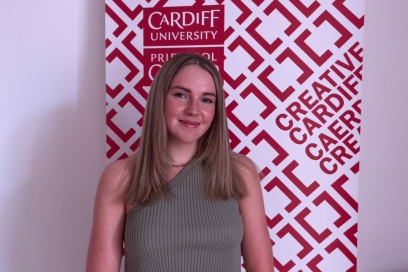 Llun o Katie yn gwenu drws nesaf i arwydd Caerdydd Creadigol